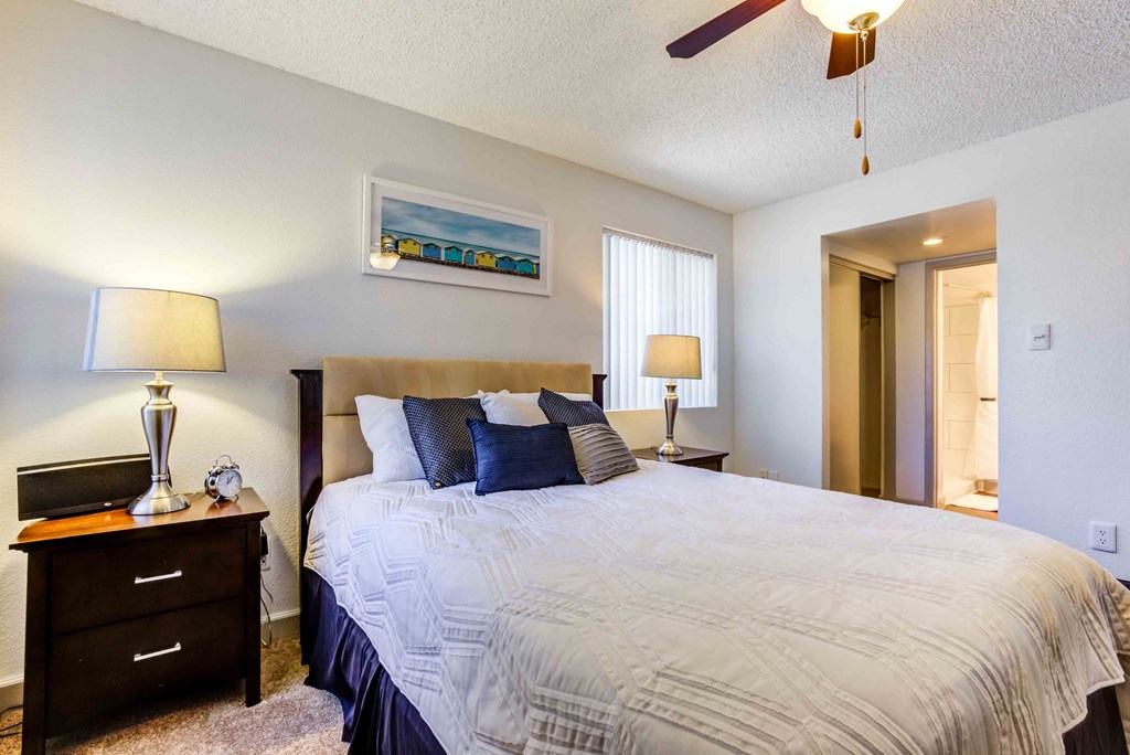 One Bedroom Apartments in Scottsdale, AZ- The Sycamore at Scottsdale - Furnished Bedroom with Plush Carpet Flooring, a Ceiling Fan, a Window, a Closet, and a Bathroom