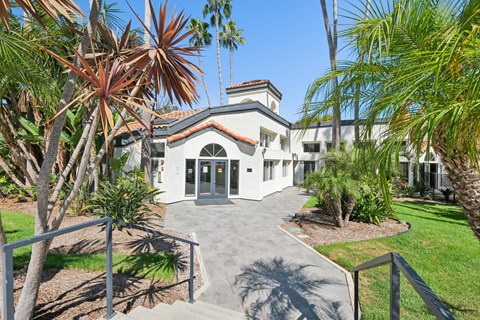 A white building with a red roof is surrounded by palm trees.