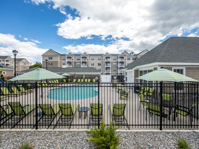 a pool with green chairs and umbrellas in front of a building