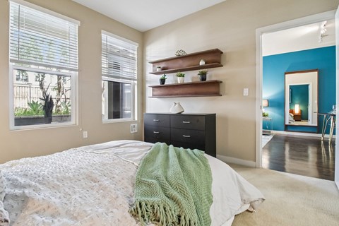 Pet-Friendly Apartments in Santa Clara, CA - Villas on the Boulevard - Bedroom Suite With Plush Carpet, Desk Nook, Bedside Lighting, Abstract Wall Art, And Direct Hallway View To Bathroom Vanity.