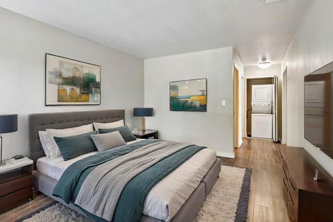 Apartments for Rent in Walnut Creek, CA - Park Lake at Walnut Creek - Bedroom With Tufted Headboard, Wood-Style Flooring, Bedside Lamps, Wall-Mounted Television, Dresser, and View of Laundry Closet.