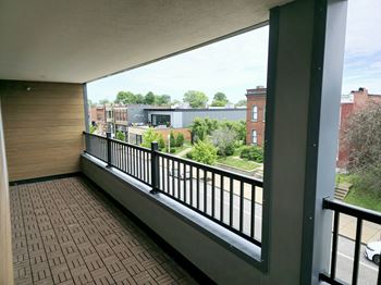 A balcony with a black railing and a view of a street with cars and buildings.