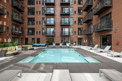 A large outdoor pool area with sun loungers and balconies of apartment buildings.