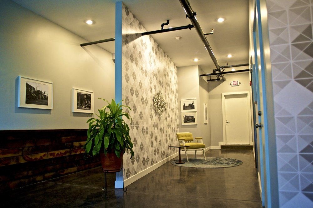 A hallway with a plant, pictures, and a yellow chair.