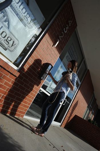 A woman is standing outside a building with a sign that reads "Ology".