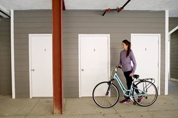 A girl with a bike stands in front of three numbered doors.