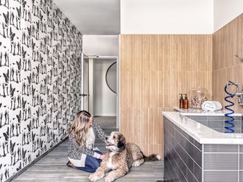 A woman is sitting on the floor with her dog in a bathroom.