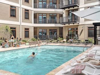A person swims in a pool surrounded by lounge chairs.