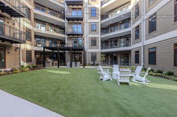 A large grassy area with four white chairs in front of apartment buildings.