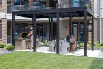 A man grilling food on a patio with two women sitting at a table.