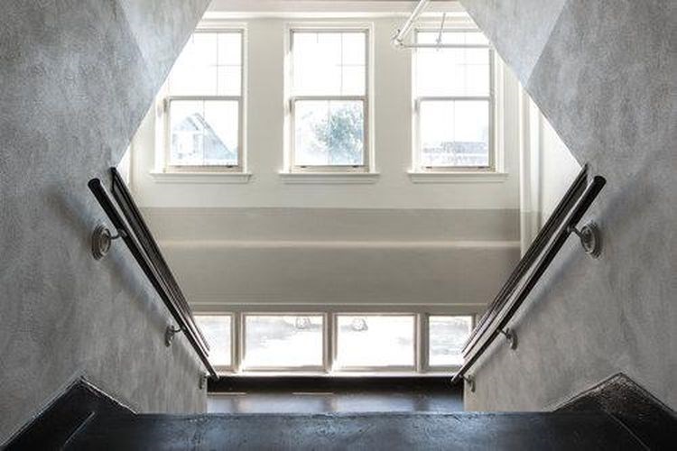 A staircase with a black railing leads to a bright room with three windows.