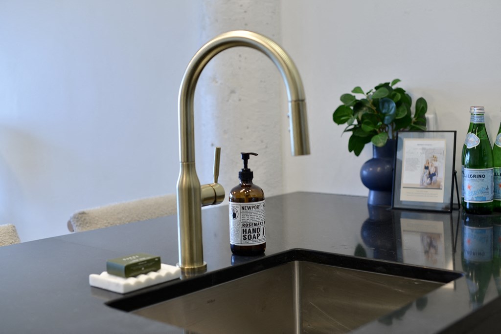 a kitchen sink with a gold faucet and a bottle of soap on it