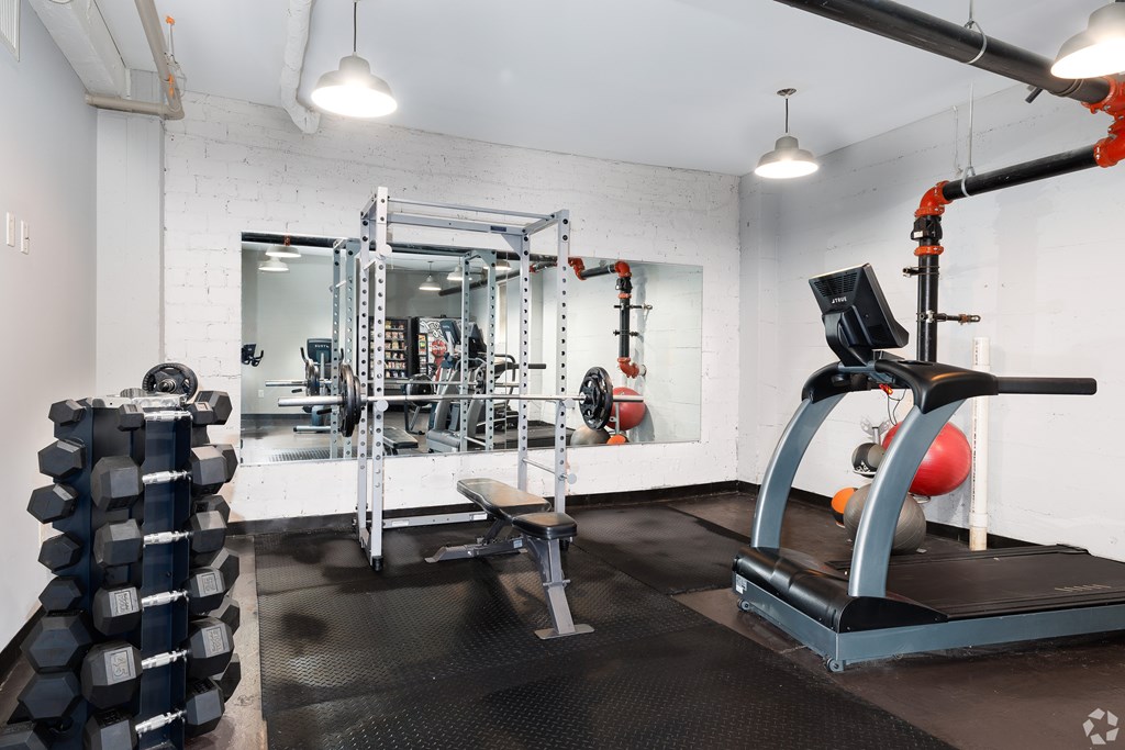 A gym with a treadmill, weight rack, and mirrors.
