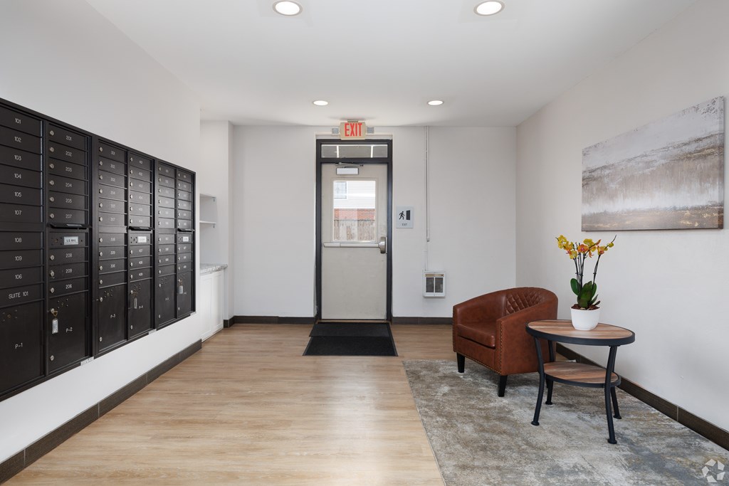 A hallway with a brown chair, a table with a vase of flowers, and a wall with a painting.