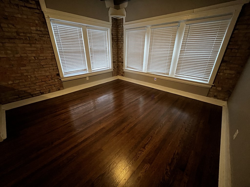 an empty living room with wood floors and a brick wall