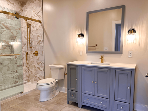 A bathroom with a marble shower, a toilet, a sink and a cabinet.