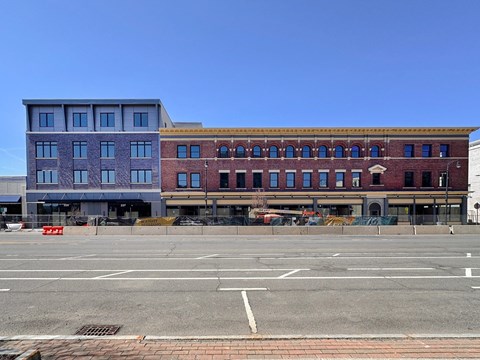 A large building with a red brick facade sits next to a smaller building with a grey facade.