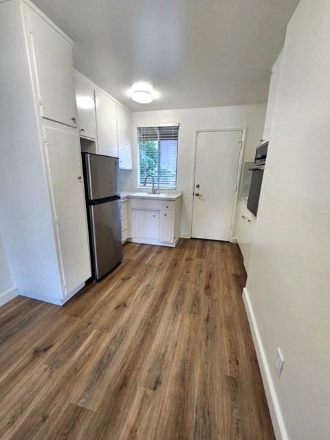 A kitchen with a refrigerator, sink, and wooden floors.