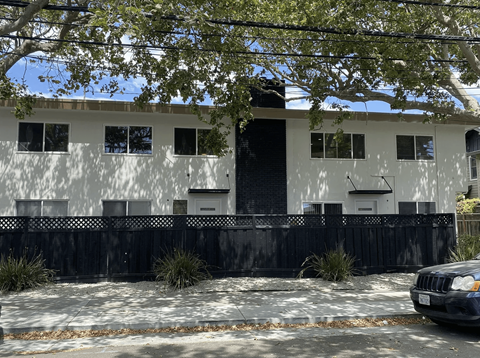 A white building with a black fence and a car parked in front.