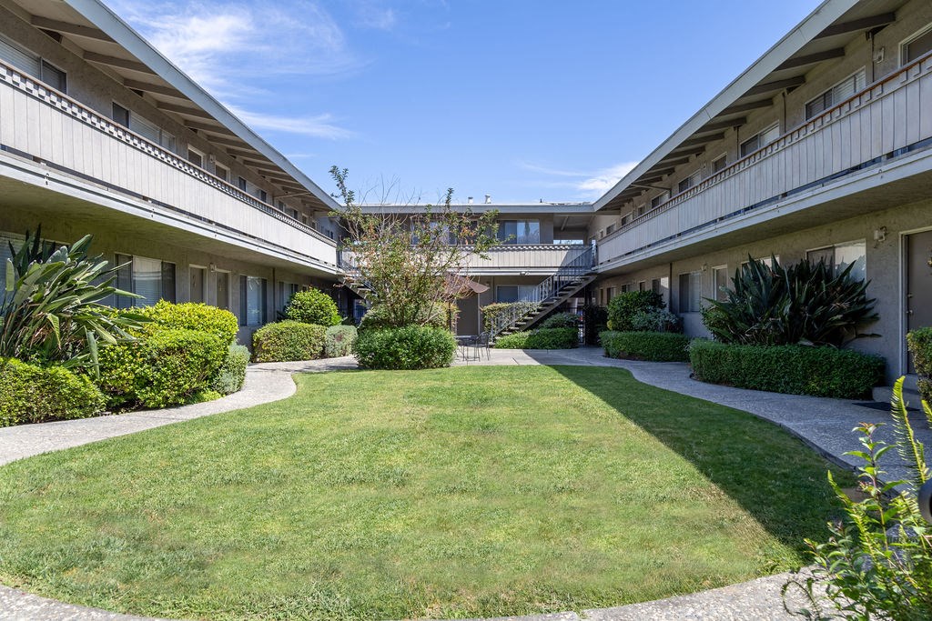 the courtyard of an apartment building with a green lawn and bushes