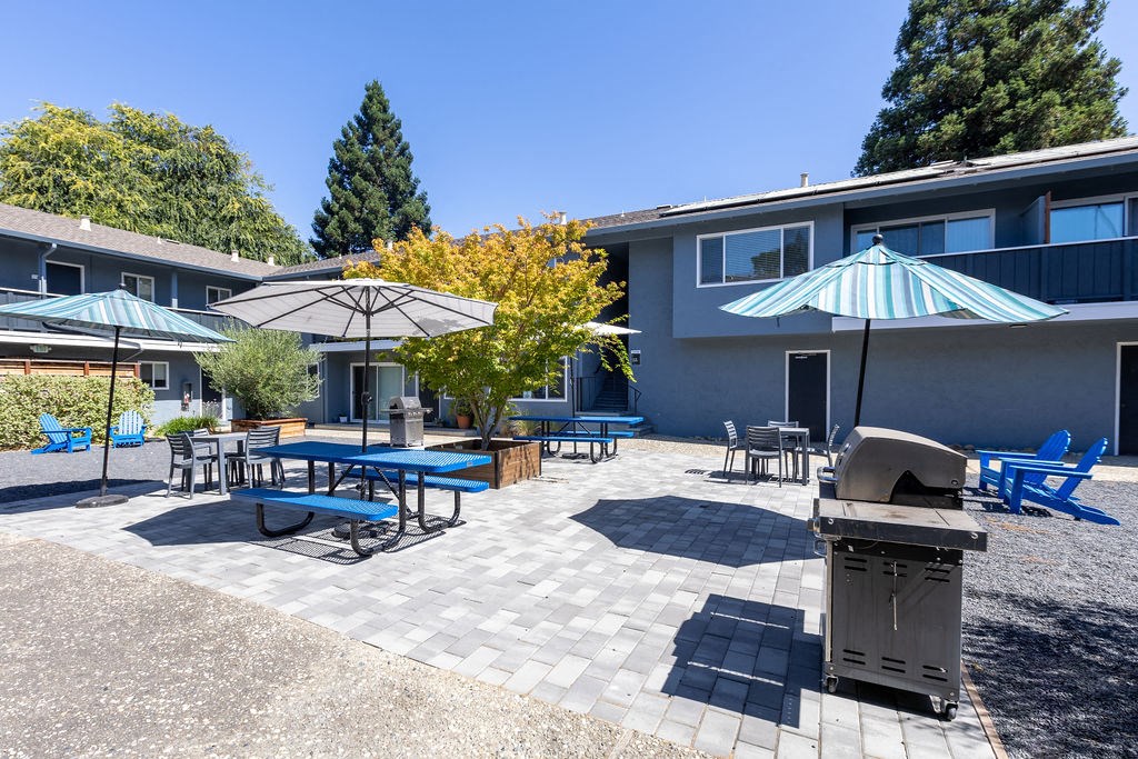 a patio with tables and umbrellas and a grill