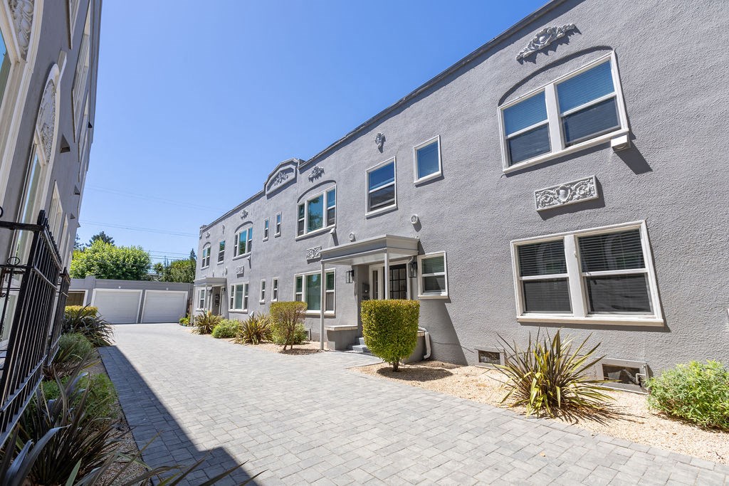 the front of a gray building with a sidewalk and a driveway
