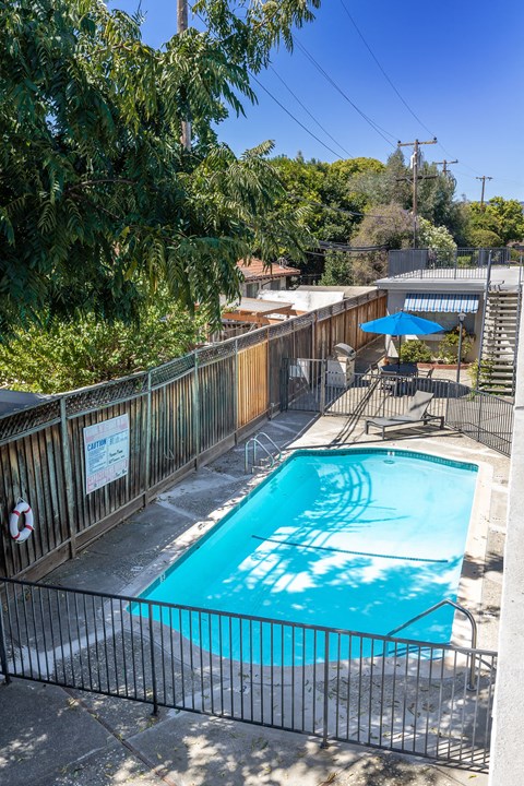 A pool surrounded by a fence with a blue umbrella in the background.