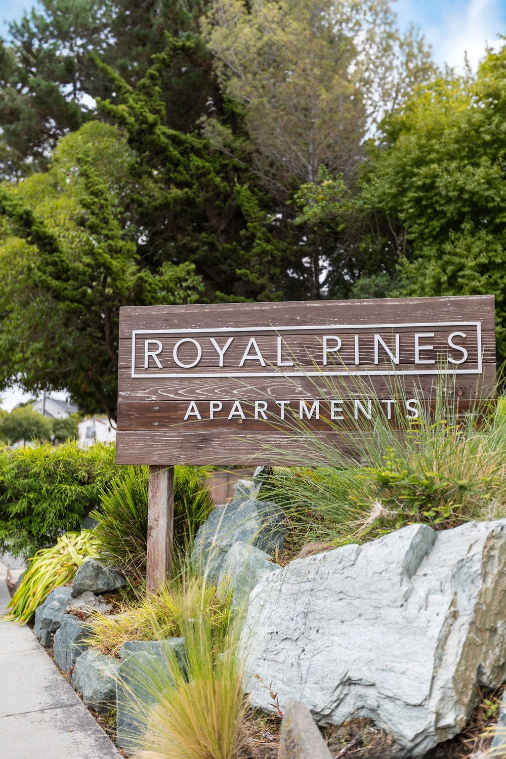 A sign that says Royal Rines Apartments in front of a green landscape.