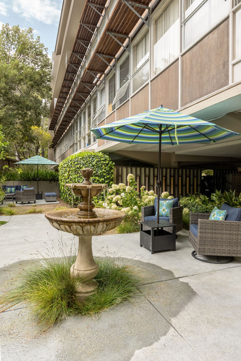 A patio with a fountain, chairs, and umbrellas.