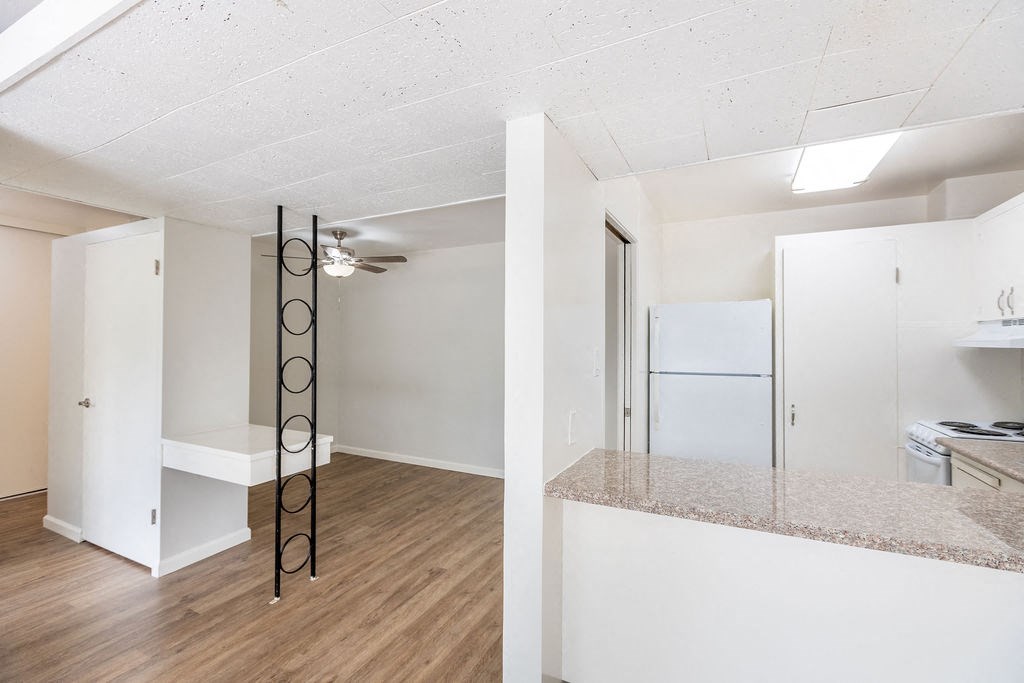 A room with a white fridge and a wooden floor.