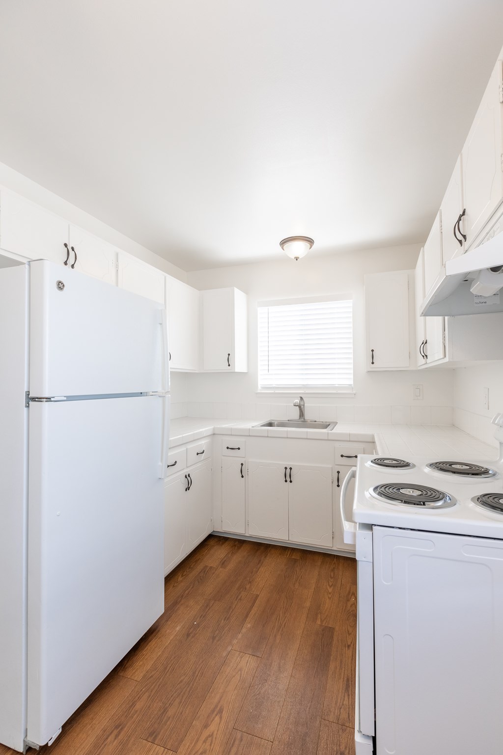 A white kitchen with a refrigerator, stove, and sink.