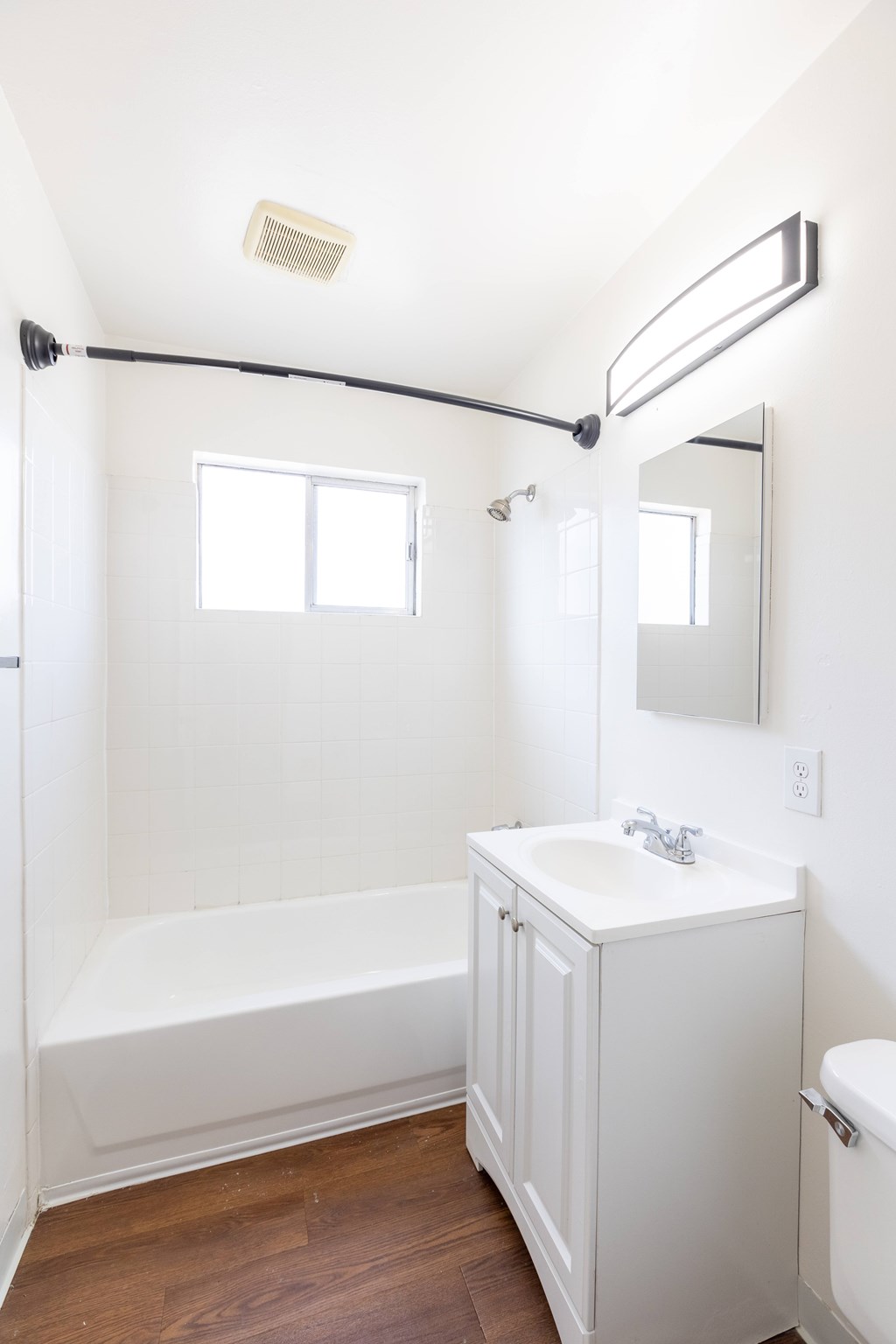 A white bathroom with a wooden floor and a window.