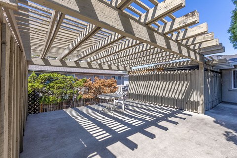 A wooden pergola over a patio with a table and chairs.