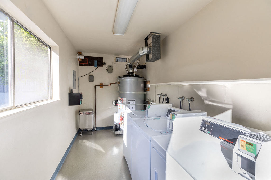 A clean, white industrial laundry room with a row of washers and dryers.