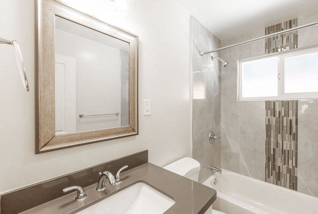 A bathroom with a sink, mirror, and bathtub.