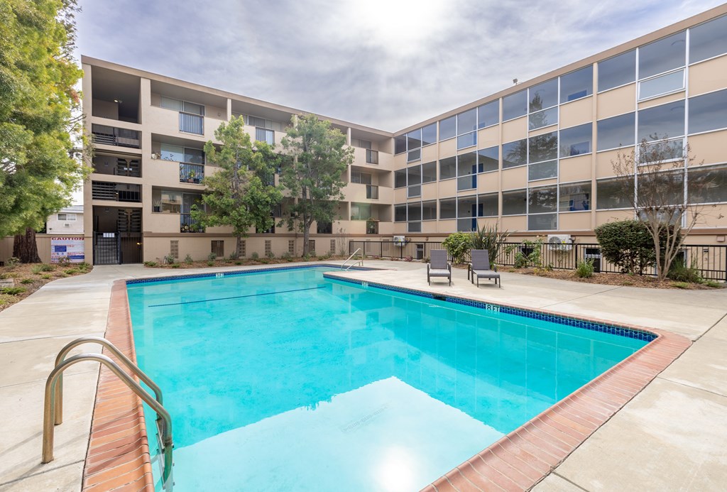 A swimming pool in front of a building with a sunny day.