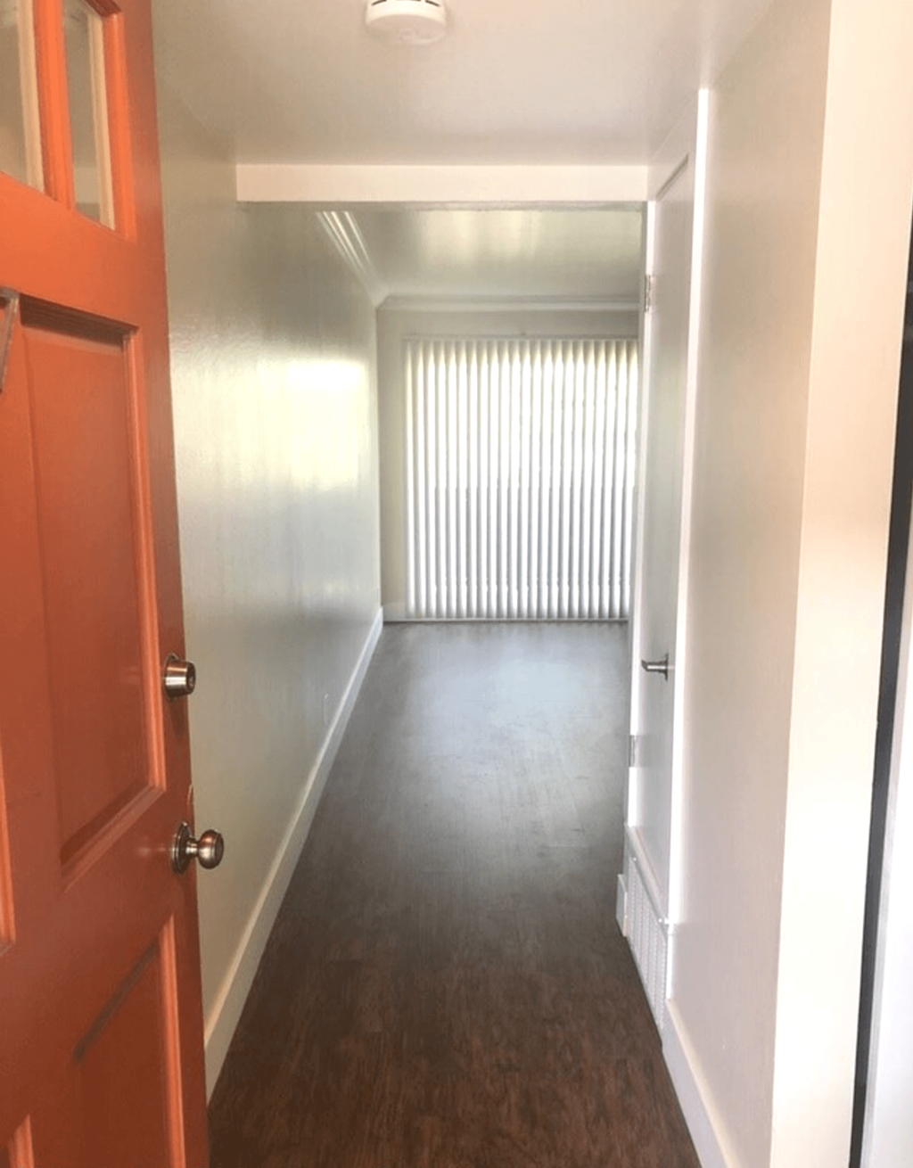 A hallway with a red door and a window with blinds.