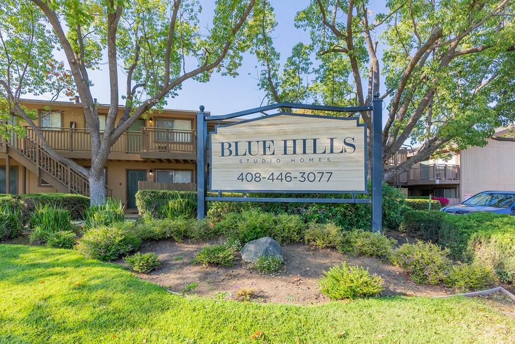 a sign for blue hills apartments with trees and a lawn