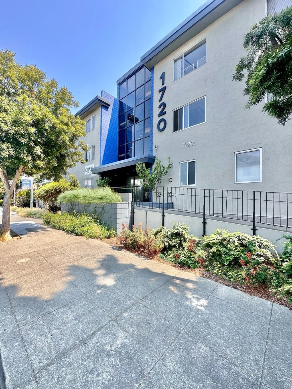 an apartment building with a sidewalk and trees in front of it