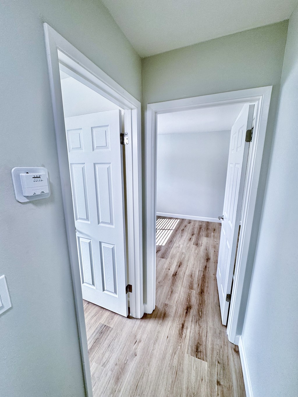 an empty room with two doors and a hallway with wood floors