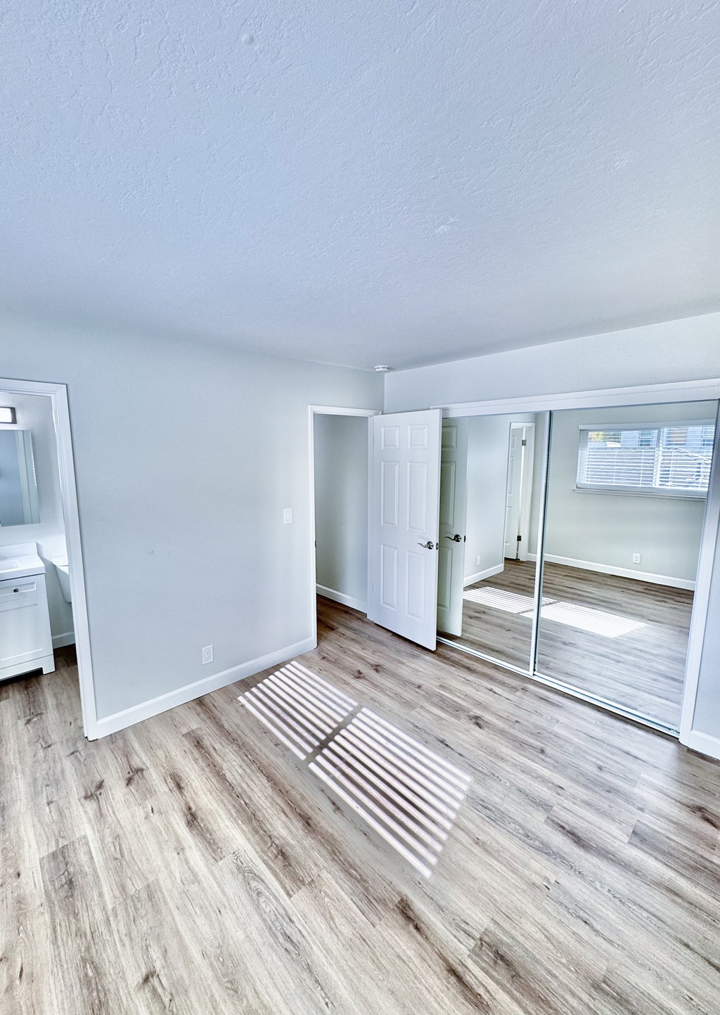the living room of an apartment with wood flooring and a mirrored closet