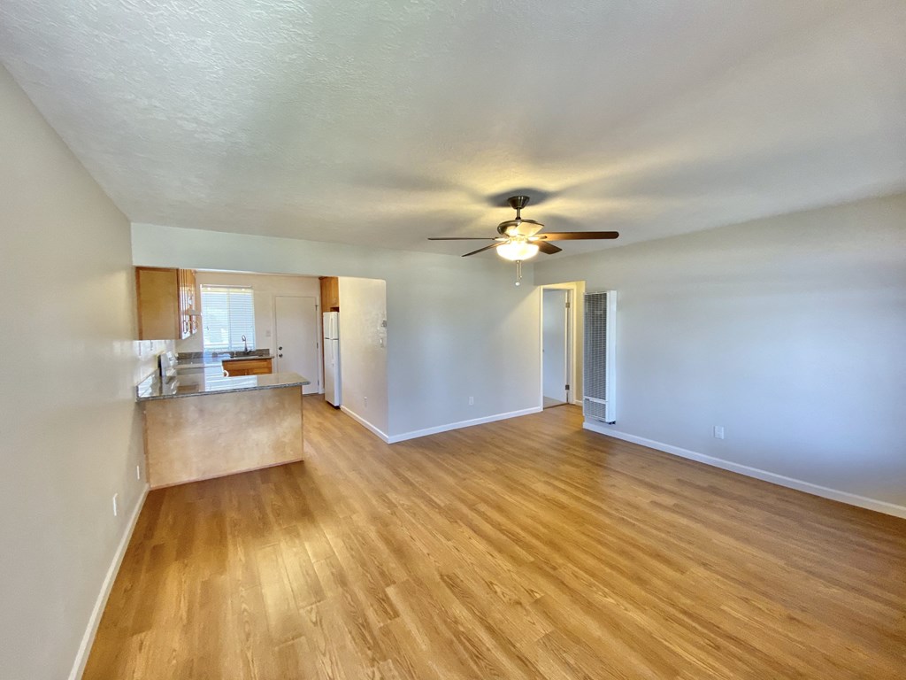 an empty living room with a ceiling fan and a kitchen