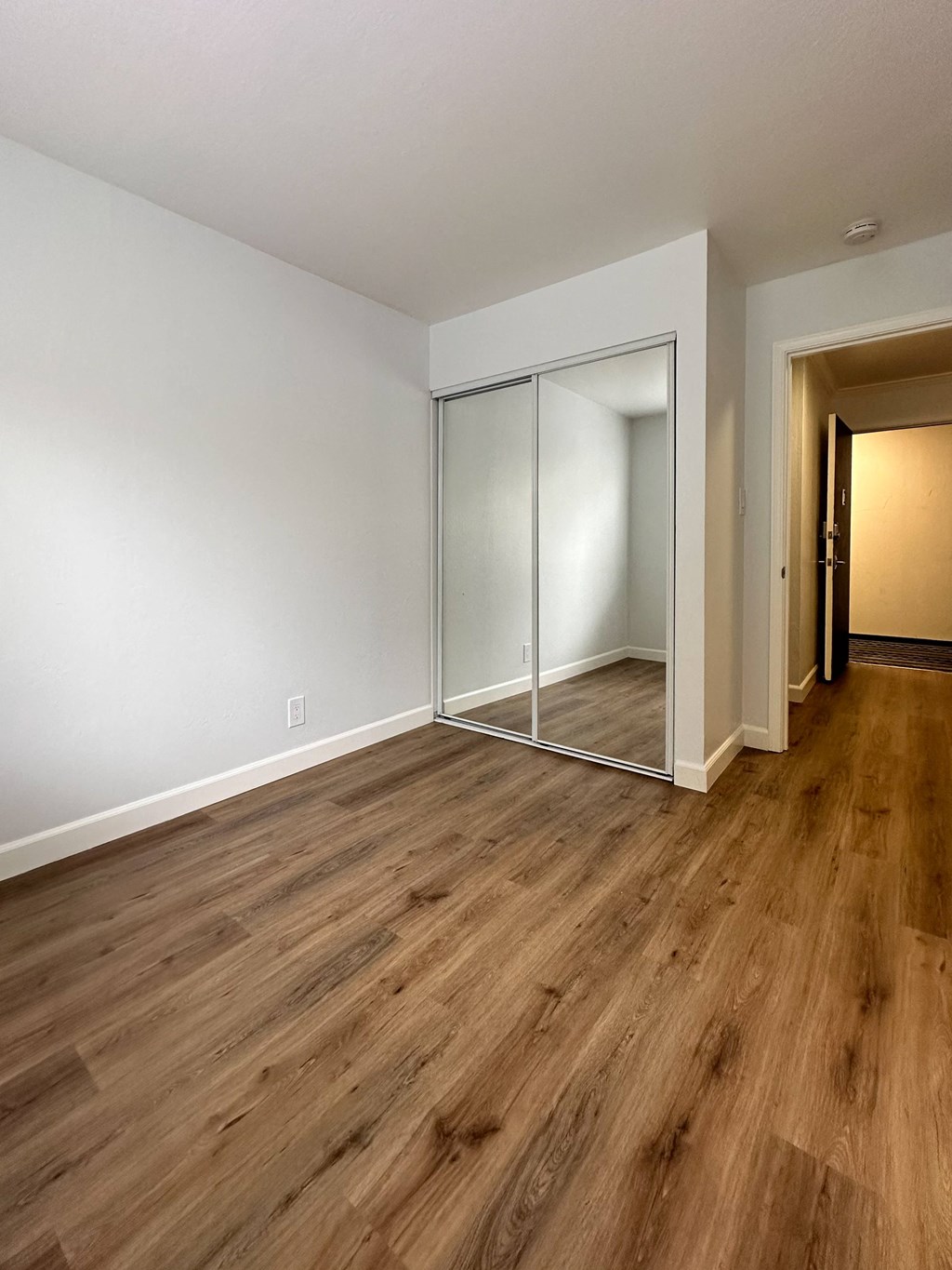 an empty living room with wood flooring and a mirrored closet at The Chase Apartment Homes, Oakland, CA 94606