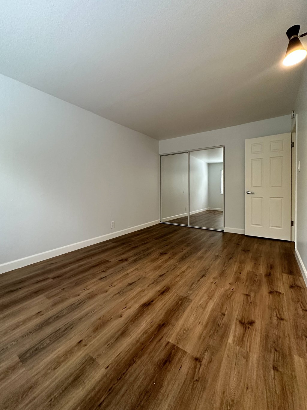 an empty living room with wood flooring and a white door at The Chase Apartment Homes, California