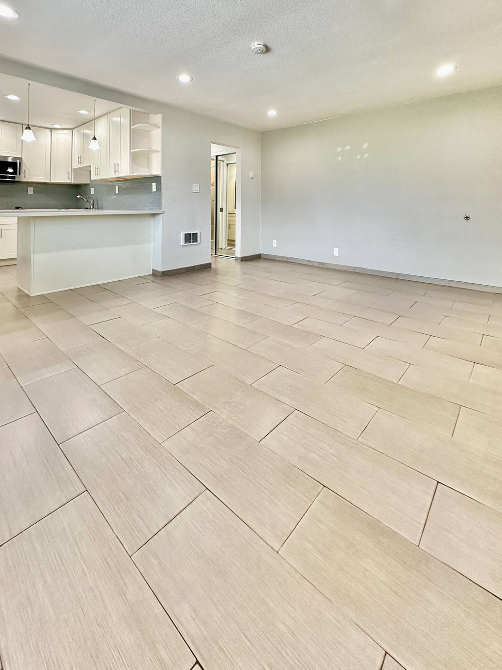 an empty living room with tile flooring and a kitchen