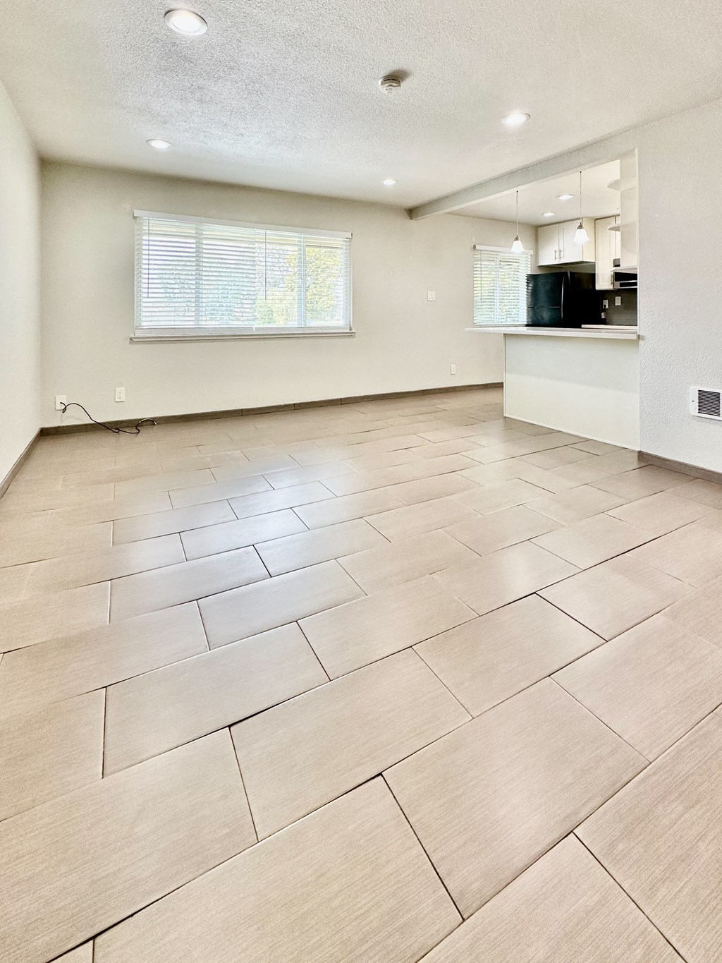 an empty living room with a kitchen and tiled floors