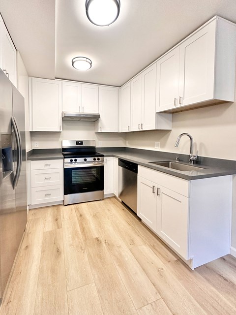 A modern kitchen with white cabinets and a wooden floor.