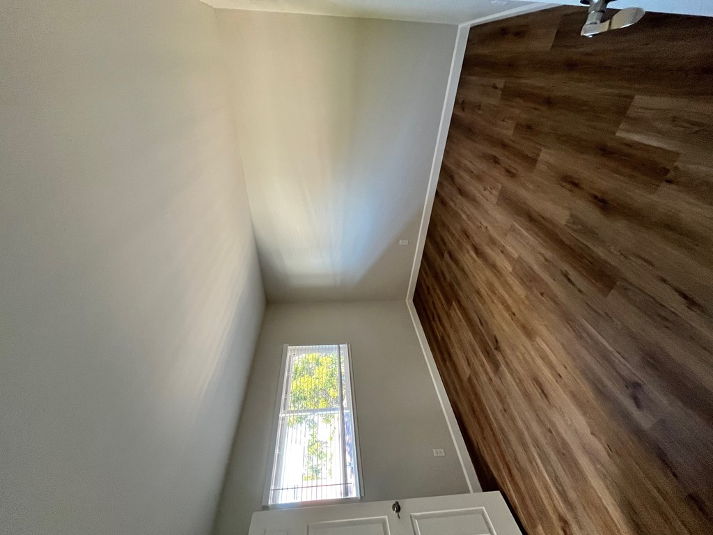 A wooden staircase with a white railing and a small window with a view of trees.