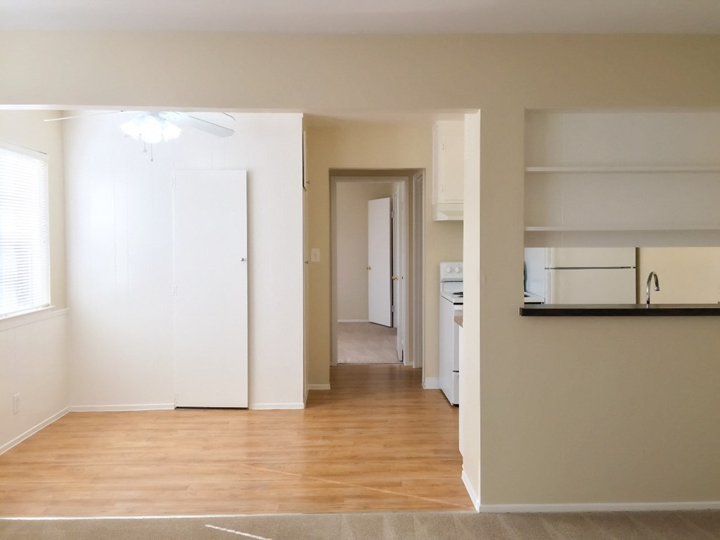 an empty living room with a hard wood floor and a hallway to a kitchen