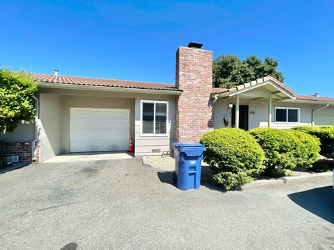 A house with a blue trash bin in front of it.